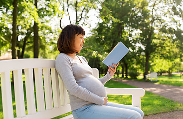 Image showing happy pregnant asian woman reading book at park