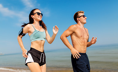 Image showing couple with phones and arm bands running on beach