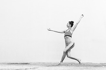 Image showing Fit sporty active girl in fashion sportswear doing yoga fitness exercise in front of gray wall, outdoor sports, urban style. Black and white photo.