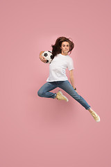 Image showing Forward to the victory.The young woman as soccer football player jumping and kicking the ball at studio on pink