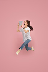Image showing Image of young woman over pink background using laptop computer or tablet gadget while jumping.