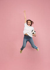 Image showing Forward to the victory.The young woman as soccer football player jumping and kicking the ball at studio on pink