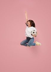 Image showing Forward to the victory.The young woman as soccer football player jumping and kicking the ball at studio on pink