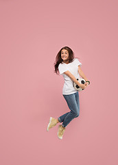 Image showing Forward to the victory.The young woman as soccer football player jumping and kicking the ball at studio on pink