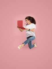 Image showing Image of young woman over pink background using laptop computer or tablet gadget while jumping.