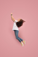 Image showing Image of young woman over pink background using laptop computer or tablet gadget while jumping.