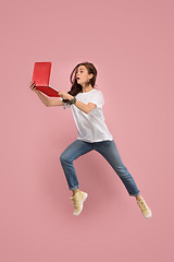 Image showing Image of young woman over pink background using laptop computer or tablet gadget while jumping.