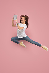 Image showing Image of young woman over pink background using laptop computer or tablet gadget while jumping.