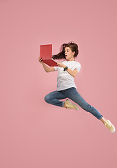 Image showing Image of young woman over pink background using laptop computer or tablet gadget while jumping.