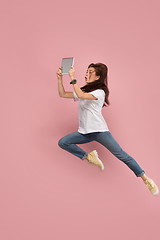 Image showing Image of young woman over pink background using laptop computer or tablet gadget while jumping.