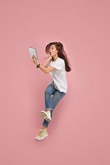 Image showing Image of young woman over pink background using laptop computer or tablet gadget while jumping.