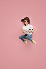 Image showing Forward to the victory.The young woman as soccer football player jumping and kicking the ball at studio on pink