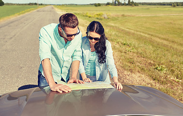 Image showing happy man and woman with road map on car hood