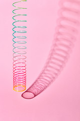 Image showing Vertical stretching plastic slinky toy with curved shadow.