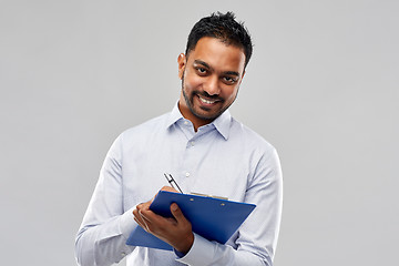 Image showing smiling indian businessman writing to clipboard