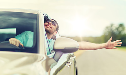 Image showing happy man in shades driving car and waving hand