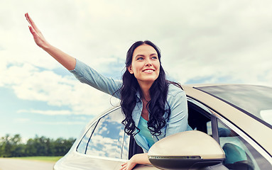 Image showing happy young woman driving in car and waving hand