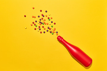 Image showing Red painted champagne bottle with colorful candies.