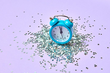 Image showing Blue vintage alarm clock on a lavender background with silver glitter.