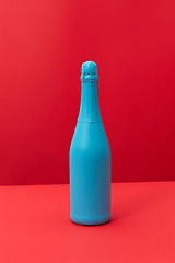 Image showing Blue painted spray wine bottle on a duotone red background.