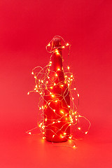 Image showing Painted red wine bottle covered Christmas garland with lights.