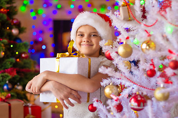 Image showing The girl at the Christmas tree holds a big gift in her hands