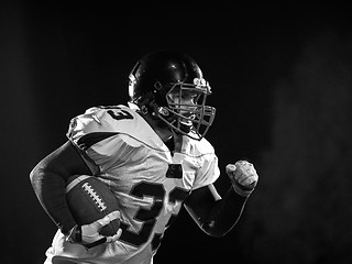 Image showing American football player holding ball while running on field