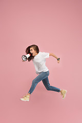 Image showing Beautiful young woman jumping with megaphone isolated over pink background