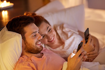 Image showing happy couple using smartphones in bed at night