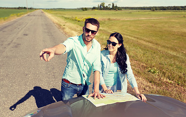 Image showing happy man and woman with road map on car hood