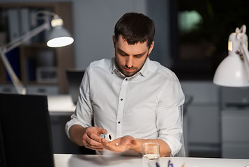 Image showing businessman taking medicine pills at night office