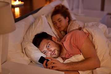 Image showing man using smartphone while girlfriend is sleeping