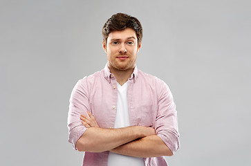 Image showing indifferent young man with crossed hands over grey