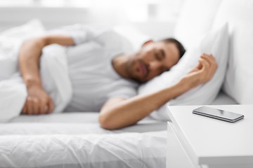 Image showing smartphone on bedside table near sleeping man