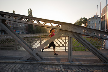 Image showing woman jogging across the bridge at sunny morning