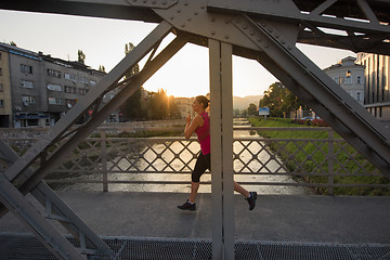 Image showing woman jogging across the bridge at sunny morning