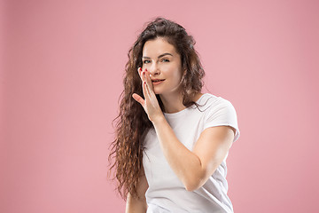 Image showing The young woman whispering a secret behind her hand over pink background