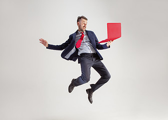 Image showing Image of young man over white background using laptop computer while jumping.