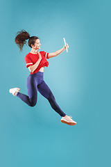 Image showing Image of young woman over pink background using laptop computer or tablet gadget while jumping.