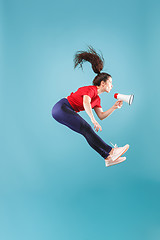 Image showing Beautiful young woman jumping with megaphone isolated over red background