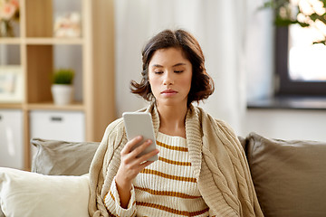 Image showing sad woman in blanket using smartphone at home