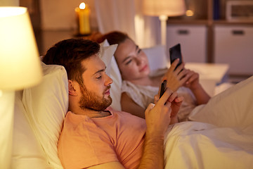 Image showing couple using smartphones in bed at night