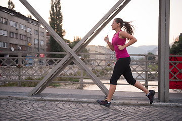 Image showing woman jogging across the bridge at sunny morning