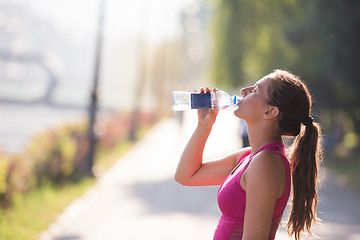 Image showing woman drinking water from a bottle after jogging