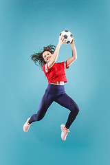 Image showing Forward to the victory.The young woman as soccer football player jumping and kicking the ball at studio on pink