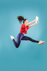 Image showing Image of young woman over pink background using laptop computer or tablet gadget while jumping.