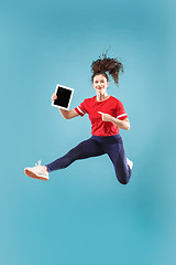 Image showing Image of young woman over pink background using laptop computer or tablet gadget while jumping.