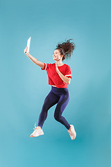 Image showing Image of young woman over pink background using laptop computer or tablet gadget while jumping.