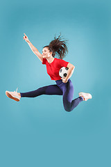 Image showing Forward to the victory.The young woman as soccer football player jumping and kicking the ball at studio on pink