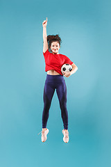 Image showing Forward to the victory.The young woman as soccer football player jumping and kicking the ball at studio on pink